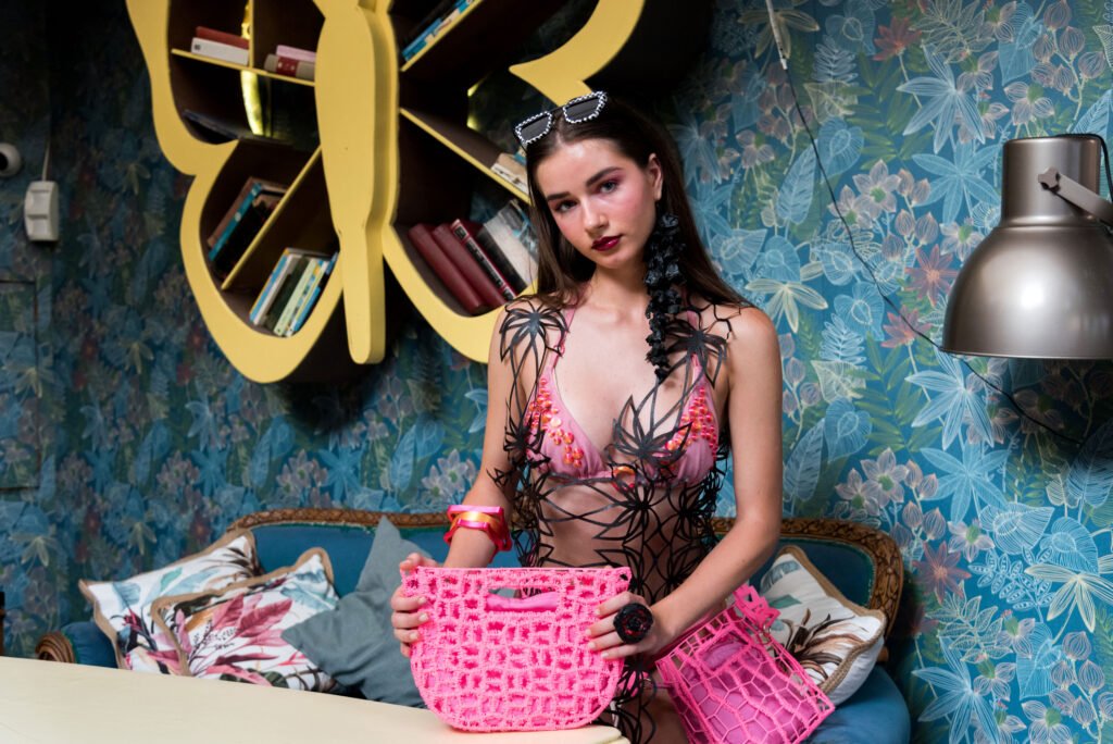 modelo luciendo un total look de nodos by g combinando el chaleco flores en 3D negro y el set de bikini rosa. Completado con el cojunto de bolsos moon y tube en fucsia y las pulseras nova y bulle en el mismo color 